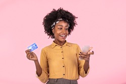 Portrait of a African American woman standing on a pink background holding smartphone and money, cashback. woman holding money and paying online on her mobile phone