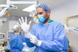 Portrait of male doctor surgeon putting on medical gloves standing in operation room. Surgeon at modern operating room
