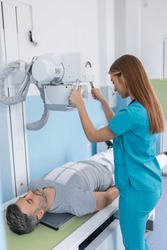 Female doctor sets up the machine to x-ray over patient. Radiologist and patient in a x-ray room. Classic ceiling-mounted x-ray system. Medical equipment