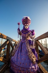 Beautiful colored carnival costume on the street in Venice. Carnival of Venice. Woman in purple dress near sea and gondola