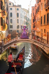 A woman in a purple dress stands on a bridge across the canal in Venice between the clutches. Beautiful colored carnival costume on the street in Venice. Carnival of Venice. Woman in purple dress.