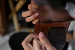a man with threads and needle , making leather goods with handstitched process