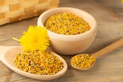 Macro shot of bee pollen or perga in wooden spoon on blurred rustic background. Raw brown, yellow, orange and blue flower pollen grains or bee bread. Healthy food supplement with selective focus