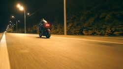 Man riding fast on modern sport motorbike at nighty city street. Motorcyclist racing his motorcycle on empty road. Guy driving bike at dusk. Concept of freedom and adventure. Low angle of view Closeup
