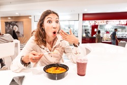 A woman eating too hot and peppery soup in an Asian fast food restaurant. Concept of spices in Oriental cuisine