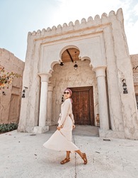 Woman tourist wearing red turban and biege long dress walks through the old narrow streets of Bur Dubai and Creek. Travel and sightseeing concept