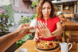 Woman refuses salt and seasonings with a gesture indicating that she is on a diet and prohibited from using ingredients harmful to health.