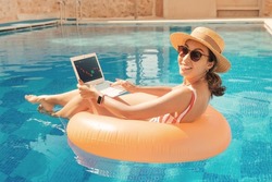 Woman with inflatable circle in swimming pool and manages her shares and other investment assets in the trading terminal with the japanese candlestick chart. Dividends and passive income concept