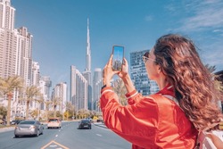 Tourist happy girl taking photos for her travel blog, in Dubai downtown district against background of the Burj Khalifa highest skyscraper
