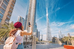 happy tourist asian girl taking photos for her travel blog, in Dubai downtown district against background of the grandiose Burj Khalifa highest skyscraper in the world