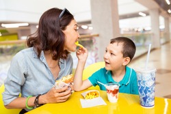 Mom and son eat fried sweet potatoes indoors. Junk and fast food concept.