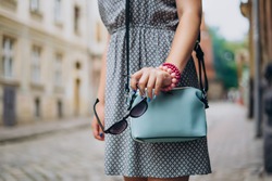 Female hand with blue handbag. Female hand with manicure and bracelets holding sunglasses. Stylish woman in dress with accessories