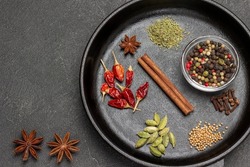 Cinnamon stick, coriander seeds, pepper pods, cardamom and allspice in frying pan. Star anise on table. Top view. Black background