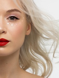 Half close-up portrait of a woman with shiny clean skin and curly blond hair. Rhinestones stars on the eyes, evening makeup and red lipstick. soft care, full lips, long eyelashes and thick eyebrows