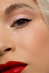 Half close-up portrait of a woman with shiny clean skin and curly blond hair. Rhinestones stars on the eyes, evening makeup and red lipstick. soft care, full lips, long eyelashes and thick eyebrows