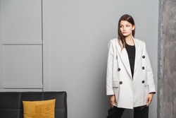 Young elegant woman in white oversize blazer and black ripped pants. Interior portrait