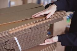 Woman taking folded stacks of corrugated cardboards for packing in warehouse, Pile of corrugated cardboard sheets and ready to use