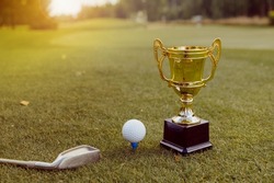 Golden winner cup with golf ball and golf club on green grass on golf course. Golf competition, sport championship
