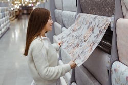 Young woman choose wallpaper in hardware store. Home design and renovation concept.