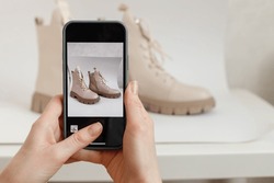 A woman takes a picture of new shoes on a mobile phone at home. Mobile shooting for goods for sale. Blogger and stylist photographing clothes. Reusing unnecessary things