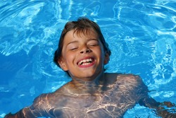 a 10-years old laughing American - German boy having fun with diving and swimming in a swimming pool, photographed in the summer sun