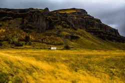 South Iceland landscape with Nupsstadur historic turf house farm in the distance at the base of the volcanic rock hills with autumn colors decorating the trees in the small forest behind the farm