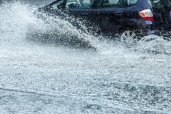car moving with high speed through water puddle on flooded city road during heavy rain