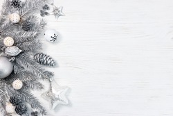 silver christmas tree branches decorated with toys, cones and garland lights on white wooden desk. holiday background.