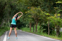 Healthy woman warming up before jogging run and relax stretching her arms and looking away in the road outdoor. Asian runner people workout fitness session, nature park background. Healthy Lifestyle 