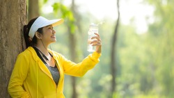 Healthy athletic asia woman is drinking pure water from the bottle refreshing herself after exercise in the nature park. Healthy and Lifestyle Concept