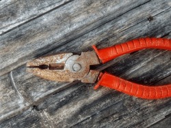 A slightly rusty pliers with a red handle on a shabby bamboo wood