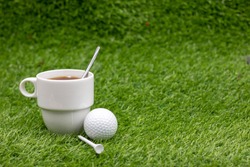 Golf ball with cup of tea on green grass, drink for golfer at club house