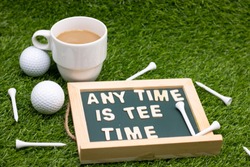 Any time is tea time on chalkboard with a cup of tea and golf ball on green grass