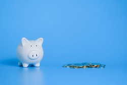 White piggy bank and many coins on blue background,investment and savings money concept.