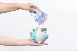 hand holding piggy bank and hand holding Colombian currency bill, money saving concept