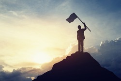 Silhouette of businessman hold a flag on top mountain, sky and sun light background. Vintage filter. Business, success, leadership, achievement and people concept.