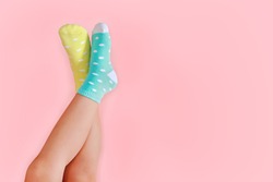 Legs with cute pastel green and yellow socks on pink background. Minimalism fashionable winter set.