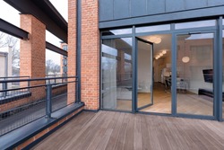 Big balcony with wooden floor and brick walls and modern loft with lights on behind window doors