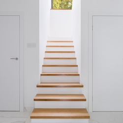 Stylish white corridor with wooden stairs, white doors and window on second floor