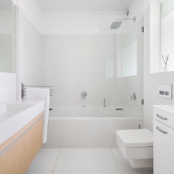 Spacious and bright bathroom with gray tiles on walls and floor and big bathtub with shower and glass wall