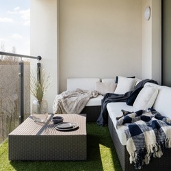 Stylish balcony with fake grass and comfortable, rattan corner sofa with pillows and blankets and square coffee table