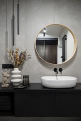 Modern classic design in bathroom with stylish decorations, big round mirror over oval, white washbasin in simple, black cabinet