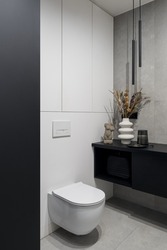 Stylish lavatory interior with white toilet, gray concrete style wall and floor tiles, modern lighting and decorations