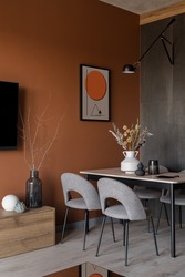 Simple dining table with elegant gray chairs in stylish room with modern art on orange wall