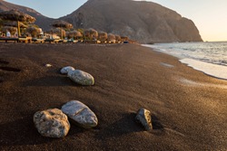 Perissa beach during sunrise on the Greek island of Santorini with sunbeds and umbrellas.