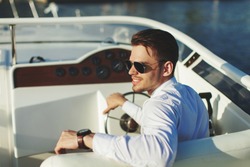 Business portrait of young smiling stylish man in suit and sunglasses driving yacht