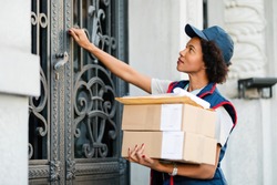 Black female courier knocking on front door while delivering packages. 