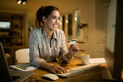 Young happy woman using credit card for online shopping in the evening at home. 