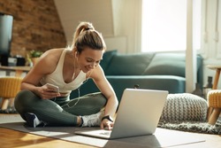 Young happy athletic woman surfing the net on laptop while taking a break from exercising at home. 