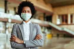 Portrait of African American woman wearing protective mask while standing with arms crossed at the airport during virus epidemic. 